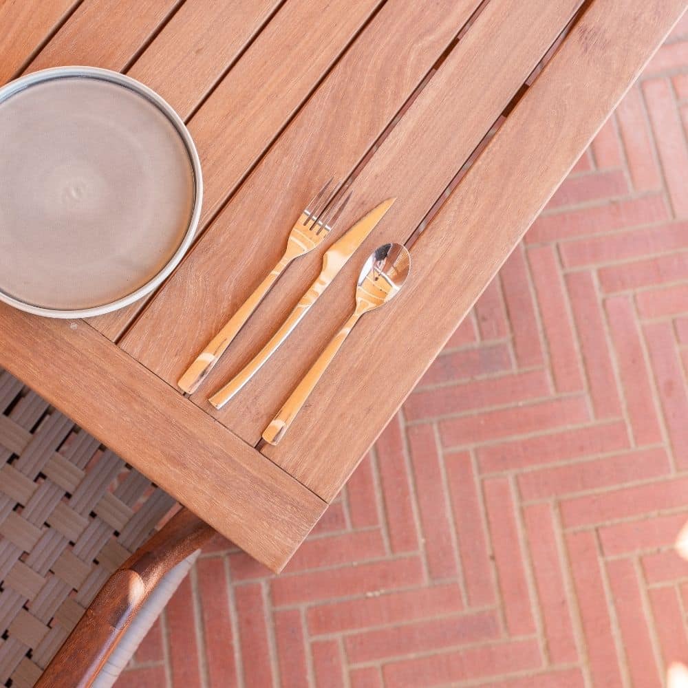 Wooden table with utensils and plate above klay paving
