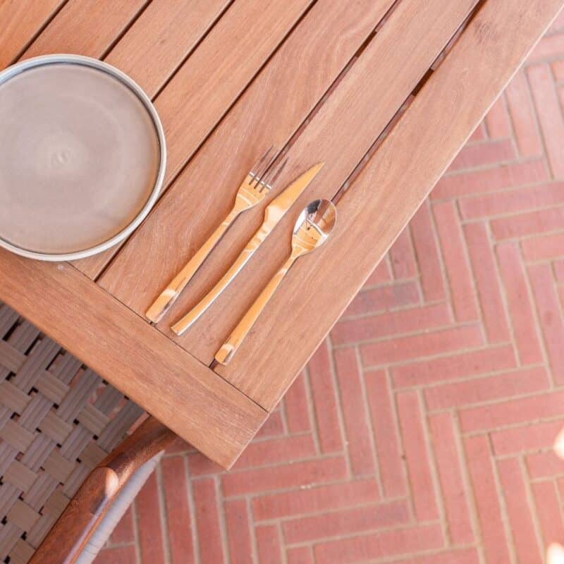 Wooden table with utensils and plate above klay paving